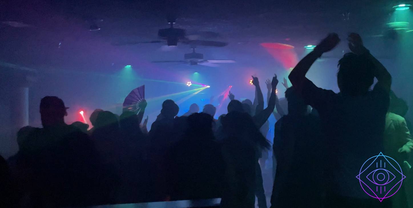 People dancing with their hands up and lasers flashing on the dance floor. 